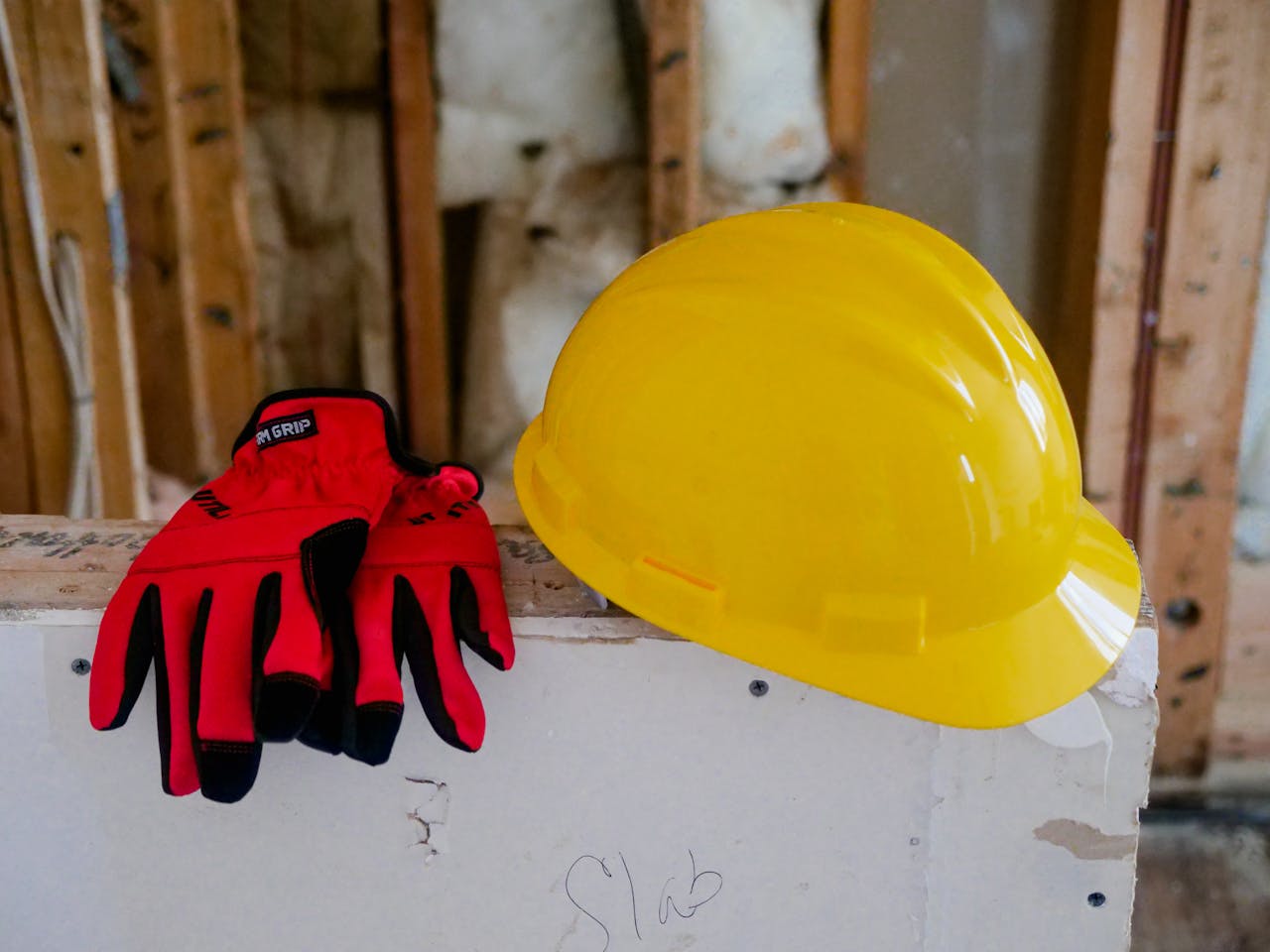 About Close-up of a yellow hard hat and red gloves on a construction site, symbolizing safety and work.